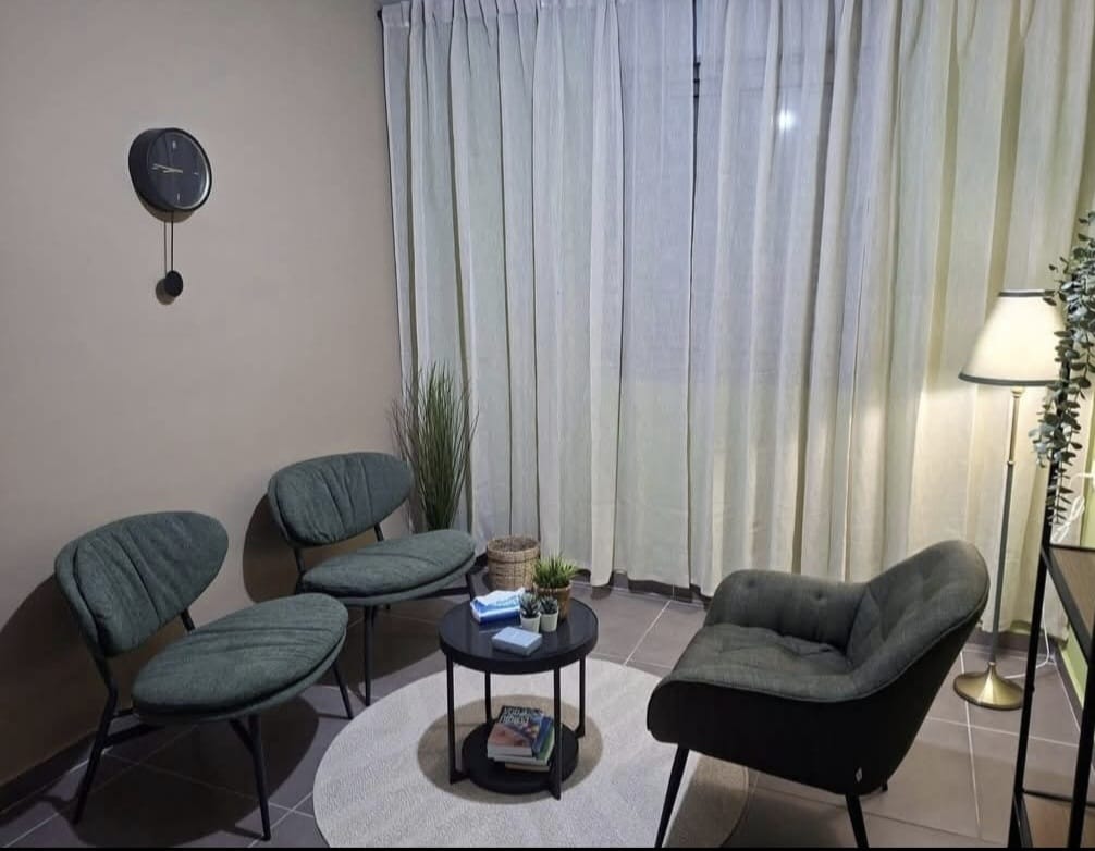 הקליניקה של שיר ברוק ברחובות: פינת ישיבה שקטה עם כיסאות, שולחן עגול, וילונות בהירים ומנורת רצפה